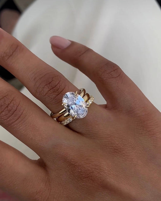 Gold ring with a large diamond on a person's finger against a neutral background